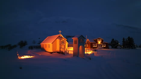 Orange-lit-church-next-to-a-hotel-in-a-thick-pack-of-snow-in-Iceland-at-night