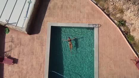 Aerial-view-of-girl-relaxing-in-a-swimming-pool-in-Spain