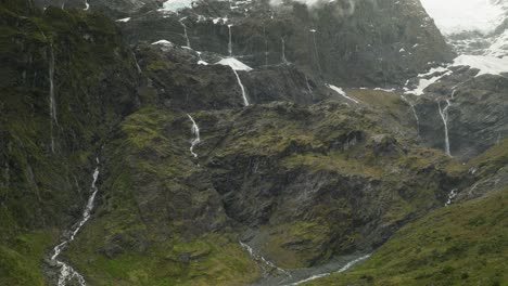 Rob-Roy-waterfalls-on-rocky-mountain-slope-below-glacier,-aerial
