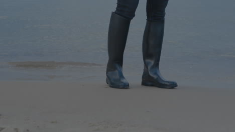 Person-with-gumboot-standing-on-sandy-beach-with-reaching-water-of-Baltic-Sea-in-background---Slow-motion-low-angle-shot