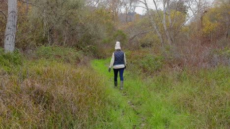 Woman-in-stocking-cap-walking-through-lush,-damp-woods-on-a-cloudy,-January-day