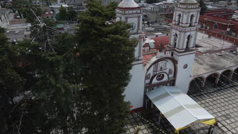 Drohne-Umkreist-Die-Kirche,-Die-Auf-Dem-Dach-Fliegt,-Panoramablick-Bei-Sonnenuntergang-Mit-Urbanen-Architekturen,-Die-Hinter-Den-Bäumen-In-Mexiko-Vorbeiziehen