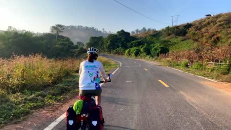 Women-cycling-in-the-sunset-road-of-Nan-province,-Thailand