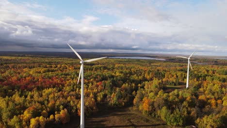Stormy-clouds-coming-over-wind-turbines-and-autumn-colored-forest,-aerial-view