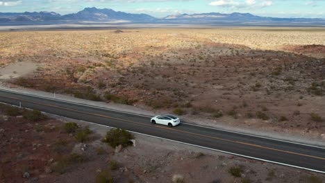 Zoom-Aéreo-Cinematográfico-De-Un-Vehículo-Eléctrico-Blanco-Moderno-Que-Viaja-Por-Una-Carretera-Vacía-En-Un-Día-Soleado-En-Nevada