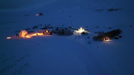Pequeña-Iglesia-Naranja-Iluminada-Al-Lado-De-Un-Hotel-En-Mucha-Nieve-En-Islandia-Por-La-Noche