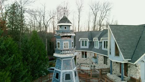 cinematic-aerial-orbiting-around-large-blue-mansion-with-a-private-lighthouse-sorounded-by-green-trees-in-Wisconsin,-USA