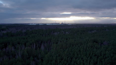 Luftfliegen-über-Waldlandschaft-Mit-Industriellen-Öllagertanks-Im-Hintergrund-An-Launisch-Bewölktem-Nachmittag