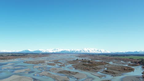 Aerial-traverse-across-beautiful-Rakaia-River-with-majestic-southern-alps-in-background-on-a-clear,-calm-mid-winter's-day