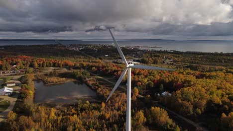 Wind-turbine-spin-while-storm-clouds-flow-over-Mackinaw-township-in-horizon,-aerial-view