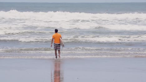 Surfista-Con-Camisa-Naranja-Camina-Hacia-La-Orilla-En-Costa-Rica