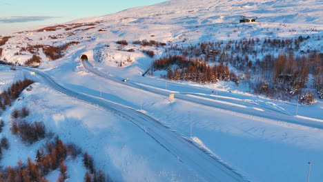 Car-drives-on-snowy-roads-in-a-white-winter-landscape-into-the-Akureyri-tunnel-illuminated-by-the-setting-sun