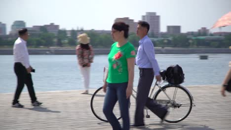 A-north-Korean-businessman-with-a-bicycle-walks-through-a-crowd-of-tourists-taking-pictures-by-the-Taedong-river-in-Pyongyang,-North-Korea