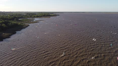Luftaufnahme-Von-Vielen-Kitesurfern,-Die-Auf-Einem-Welligen-Braunen-Fluss-An-Der-Küste-Von-Buenos-Aires-Surfen