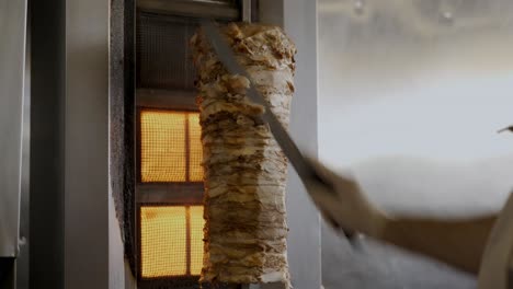 Küchenchef-Schneidet-Scheiben-Aus-Einem-Großen-Hähnchen-Shawarma-Spieß,-Der-Am-Grill-Aufgehängt-Ist