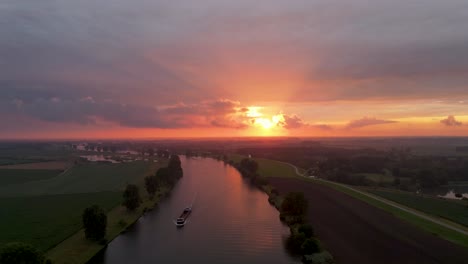 An-aerial-shot-of-a-Beautiful-sunset-over-Dutch-river-where-a-vessel-passes-by-in-an-orange-and-red-scenery