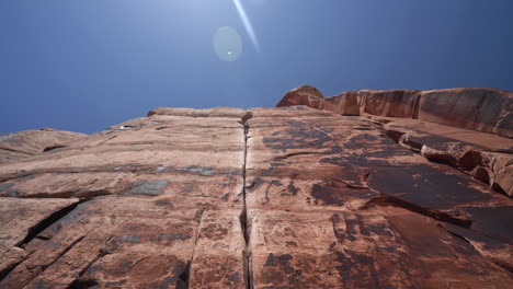 Man-Climbing-on-Steep-Red-Rock-in-Utah-USA,-Low-Angle-View-of-Climber,-Ropes-and-Cliff-on-Hot-Sunny-Day