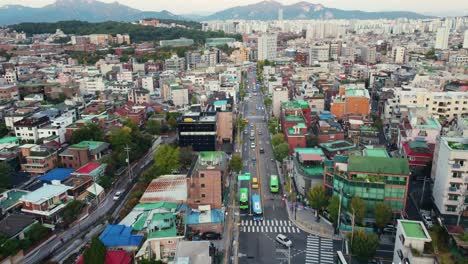 Vista-Aérea-De-Drones-De-La-Colorida-Ciudad-Asiática-En-Corea-Con-Una-Gran-Montaña-Y-Un-Bosque-En-El-Fondo