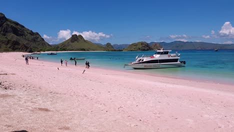 Tourist-enjoying-time-on-Pink-Beach-with-pink-sandy-beach-landscape-views,-crystal-clear-turquoise-ocean-water-and-boats-within-Komodo-National-Park-in-Indonesia