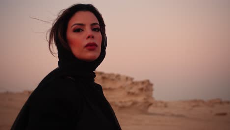 Girl-looking-straight-at-the-camera-with-innocent-eyes-holding-a-black-scarf-in-her-hands-flying-towards-the-camera-to-cover-the-lens-in-the-fossil-dunes-UAE-Dubai-Abu-Dhabi