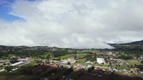 Volando-Sobre-Unos-Campos-De-Trigo-Sobre-Las-Nubes,-Situado-Cerca-De-Unos-Cerros