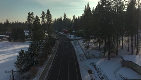 Snowy-suburban-road-at-dusk-with-light-traffic,-aerial-footage,-slow-motion