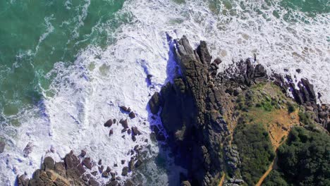 Aerial-shot-of-waves-in-Cantabria,-Spain-crashing-on-the-rocks-during-a-sunny-day
