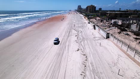 Aerial-view-of-a-car-driving-on-the-Daytona-beach,-in-sunny-Florida---reverse,-tilt,-drone-shot
