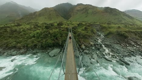 Woman-hiker-with-nordic-walking-poles-crossing-above-rapids-on-suspension-bridge