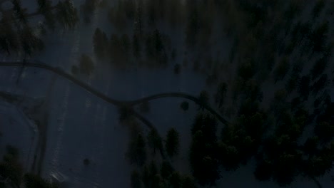 Top-down-shot-of-snowy-ranch-in-the-forest,-slowly-reveals-foggy-valley-in-distance,-aerial-footage