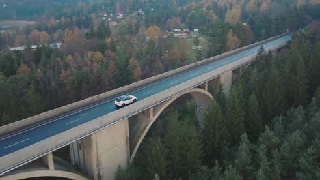 Elektroauto-Auf-Erhöhter-Brücke,-Drohnenaufnahme-Eines-Weißen-Fahrzeugs,-Das-Sich-An-Einem-Feuchten-Herbsttag-Auf-Der-Straße-Bewegt