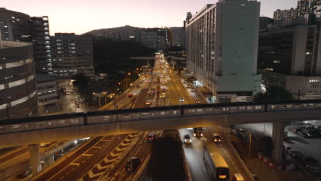 Züge,-Die-An-Einem-Klaren-Abend-In-Hong-Kong-Auf-Einer-überführung-über-Eine-Stark-Befahrene-Autobahn-Fahren