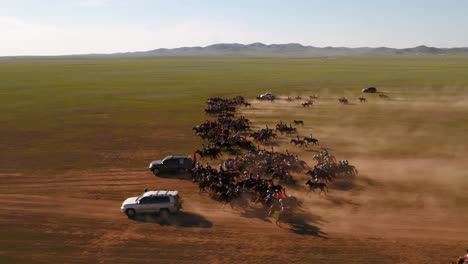 Filmische-Drohnenaufnahme-Einer-Gruppe-Von-Jockeys,-Die-In-Schnellem-Galopp-Und-Galopp-über-Die-Mongolische-Steppe-Reiten