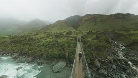 Woman-crossing-small-suspension-bridge-in-remote-rainy-valley-New-Zealand