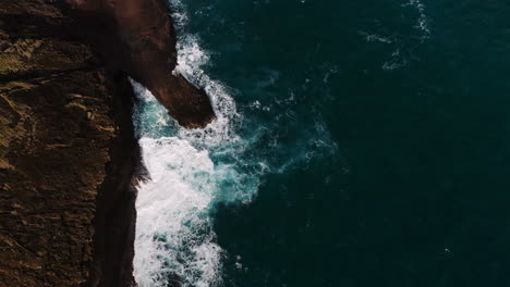 Aerial-bird's-eye-drone-shot-of-waves-crashing-against-rocky-coastline