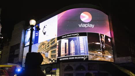 Pan-up-at-people-watching-Piccadilly-Circus-screen-in-central-London-at-night