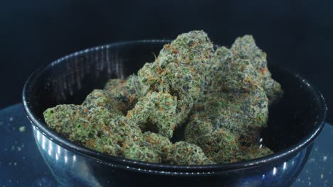 Green-Dried-Marijuana-Buds-Close-Up-concept-Shot,-pile-of-dried-marijuana-plants,-orange-trichomes-strains,-in-small-black-shiny-bawl,-on-a-rotating-stand,-studio-lights,-slow-motion,-4K-video,-smoke