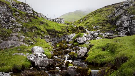 Wild-mountain-river-flowing-down-through-stones-in-cold-green-mountain-in-the-Faroe-Islands