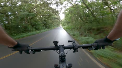 Cyclists-passing-through-wooded-country-road-after-rain,-POV-video