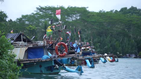 Fishermen's-boats-lean-on-the-white-sand-beach-and-the-blue-sky-of-Pangandaran,-West-Java,-Indonesia,-with-beautiful-red-and-white-flags-fluttering