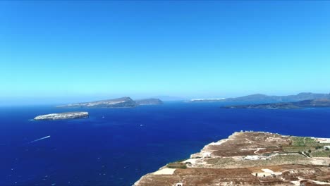 Aerial-4K-Blue-Sea-and-Sky-Top-View-of-Village-of-Akra-Mavro-Vouno-with-Oia-in-Distance-in-Santorini-Greece