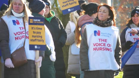 NHS-nurses-strike-for-fair-pay-salary,-waving-banners-and-flags-outside-UK-hospital