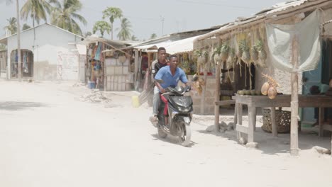 Zwei-Junge-Schwarze-Männer-Fahren-Mit-Dem-Motorrad-Durch-Das-Dorf-In-Afrika