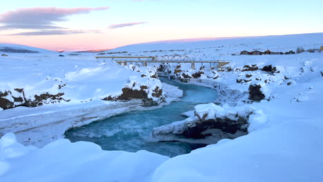 Cars-drive-over-the-bridges-of-the-Godafoss-bridges-as-the-meltwater-flows-quickly-between-the-snowy-landscape-just-after-sunset