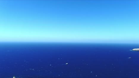 Vista-Aérea-4k-Azul-Mar-Y-Cielo-Sobre-El-Faro-Akrotiri-En-Santorini-Grecia