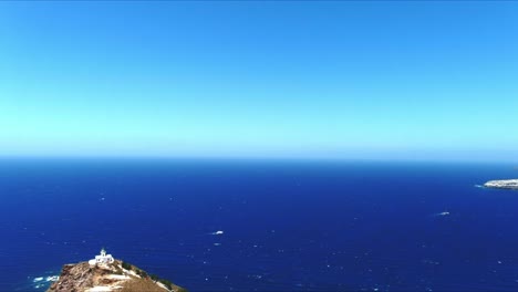 Vista-Aérea-De-4k-Azul-Mar-Y-Cielo-Sobre-El-Faro-De-Akrotiri-Con-Turbulencia-De-Viento-En-Santorini-Grecia
