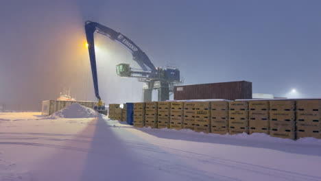 Snow-falls-in-the-port-of-Husavic-where-a-mobile-harbor-crane-stands-still-while-the-harbor-lights-are-on