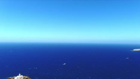 Vista-Aérea-4k-Azul-Mar-Y-Cielo-Sobre-El-Faro-Akrotiri-Cerca-De-Barcos-En-Santorini-Grecia