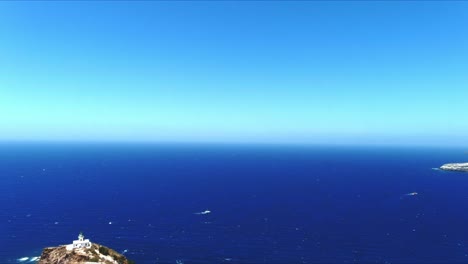 Vista-Aérea-De-4k-Azul-Del-Mar-Y-El-Cielo-Sobre-El-Faro-De-Akrotiri-Mientras-Los-Barcos-Compiten-En-Santorini,-Grecia