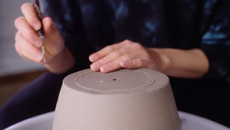 Potter-scores-clay-pot-on-pottery-wheel